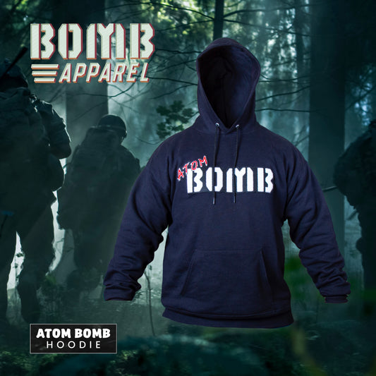 A black fleece hoodie with the Atom Bomb brand logo stitched across the chest, featuring a hood, ribbed cuffs, and a front kangaroo pocket, displayed in a forest setting with a military-themed backdrop.